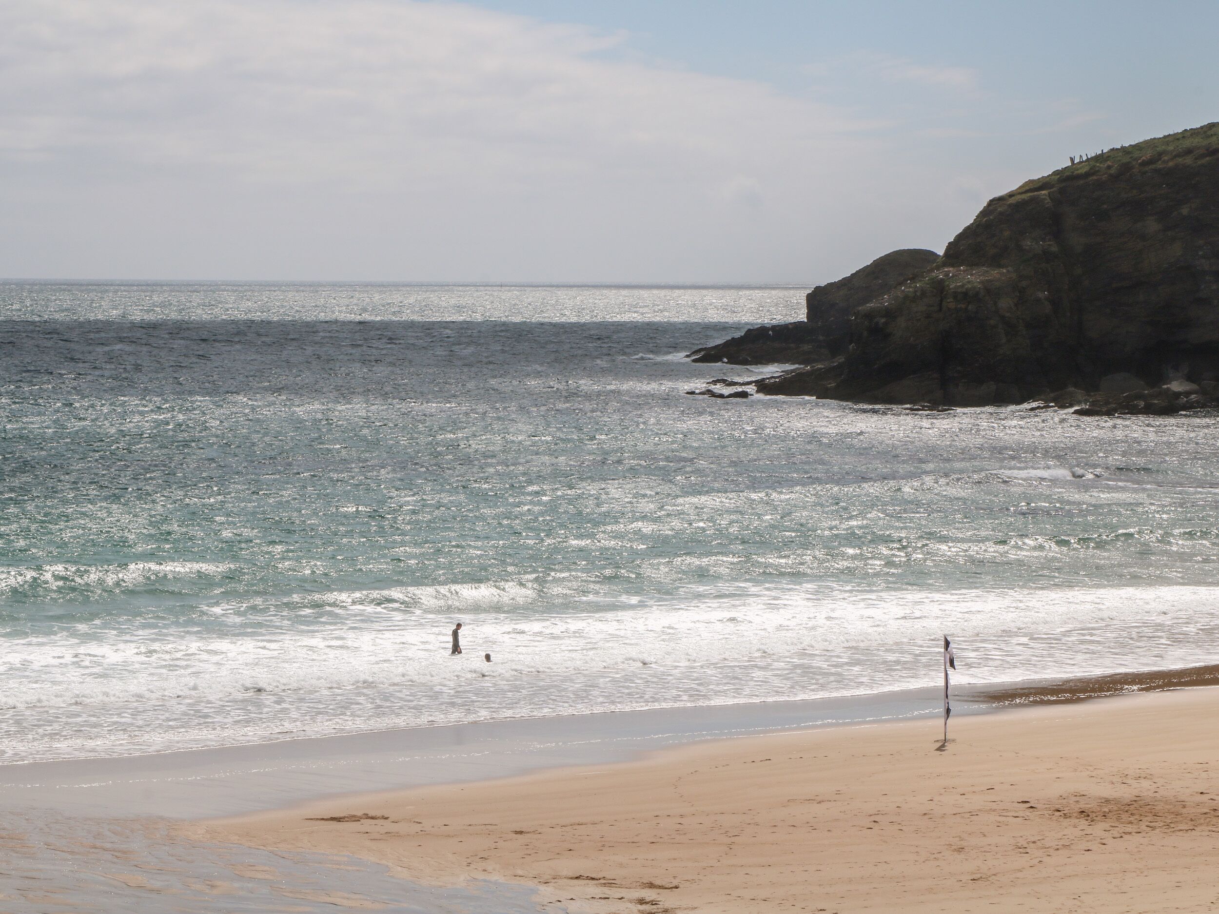 A beach with a rocky cliff, calm sea, and a clear sky.