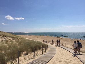 A sandy beach with a wooden boardwalk leading to the water, surrounded by dunes. - A cozy house in a central location on the Cap Ferret peninsula (Lège-Cap-Ferret)