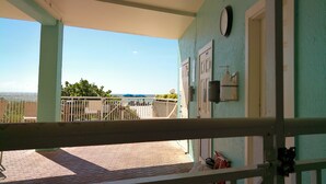 A covered outdoor area with a view of the sea, a clock on the wall, and a fire extinguisher mounted on the wall.