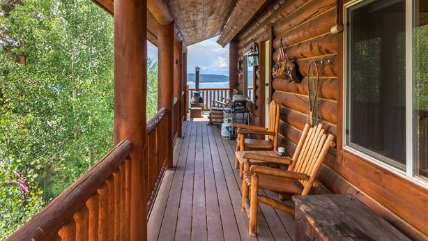 Una cabaña de madera con un porche, sillas de madera y vista al bosque.