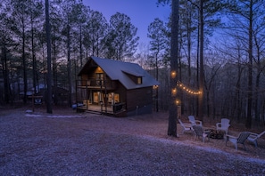 A cabin with a deck, surrounded by trees, and a fire pit with chairs. - Secluded Treehouse Cabin Near Hochatown with Hot Tub, Game Loft & Playset (Broken Bow)