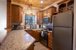 A kitchen with wooden cabinets, granite countertops, a stainless steel refrigerator, a microwave, and a stove. - Secluded Treehouse Cabin Near Hochatown with Hot Tub, Game Loft & Playset (Broken Bow)
