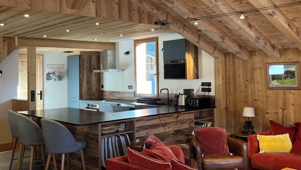 A modern kitchen with a central island, wooden ceiling beams, and a view of the outside. - Le Refuge du Cabri -15 people- sauna - jacuzzi Les Ménuires -Skis aux Pieds (LES BELLEVILLE)