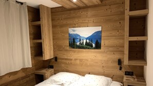 A wooden-paneled bedroom with a bed, a nightstand, a wall-mounted TV, and a curtain. - Le Refuge du Cabri -15 people- sauna - jacuzzi Les Ménuires -Skis aux Pieds (LES BELLEVILLE)