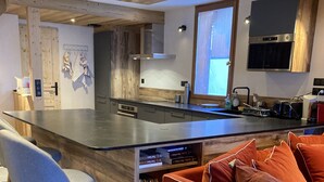 A modern kitchen with a central island, bar stools, and a sofa with cushions. - Le Refuge du Cabri -15 people- sauna - jacuzzi Les Ménuires -Skis aux Pieds (LES BELLEVILLE)