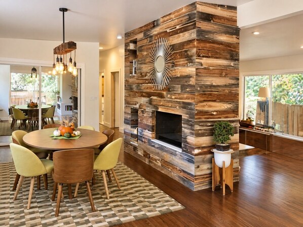 A modern living room with a wooden wall feature, a fireplace, and a dining area with chairs and a table.
