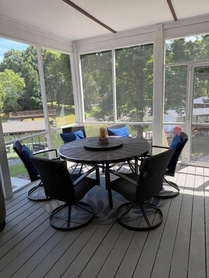 A covered patio with a round table and chairs, large windows, and a view of a backyard.