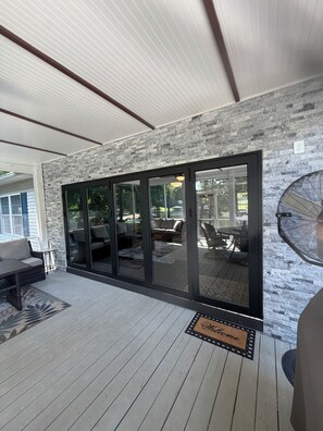 A covered patio with a stone wall, sliding glass doors, outdoor furniture, and a doormat.
