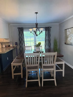A dining area with a table, chairs, a chandelier, a potted plant, and a view through large windows. - Stunning Lake Gaston waterfront! Renovated 3BR 2BA with dock on an acre lot. (Henrico)