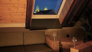 Une pièce chaleureuse avec un plafond en bois, une lucarne en verre, un canapé en cuir, une table basse en bois ornée d’un élément décoratif en verre, et une petite table avec un verre à vin.