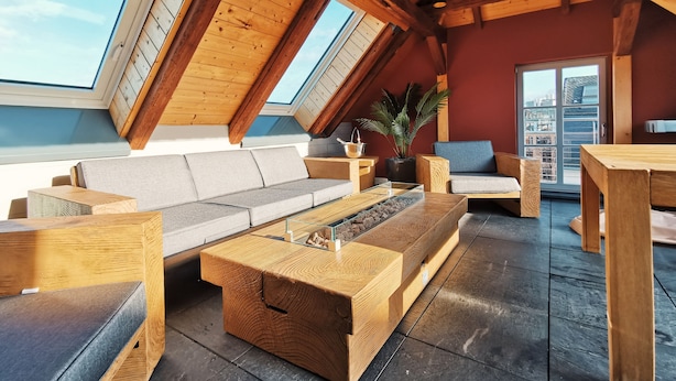 Un loft spacieux avec un plafond en pente, des poutres en bois, une grande fenêtre, un canapé, une table basse et une table à manger.