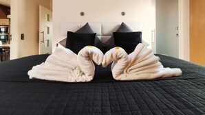 Un lit bien fait, recouvert d’une courtepointe noire, avec deux oreillers noirs et deux serviettes blanches disposées en forme de cœur.