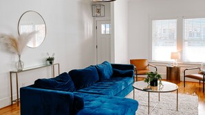 Un salon moderne avec un canapé d’angle bleu, une table basse en verre et un tapis à poils longs blanc.
