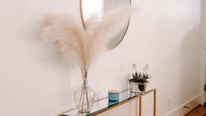 Un couloir avec une console en verre, un miroir, des plumes d’herbe de la pampa et une petite plante en pot.