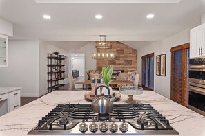 Una cocina moderna con una isla central, estufa integrada y un área de comedor al fondo.