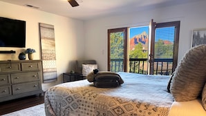 A bedroom with a large bed, a dresser, a TV, and a window with a mountain view. - Red Rock Awakening - Spacious Uptown home (Sedona)