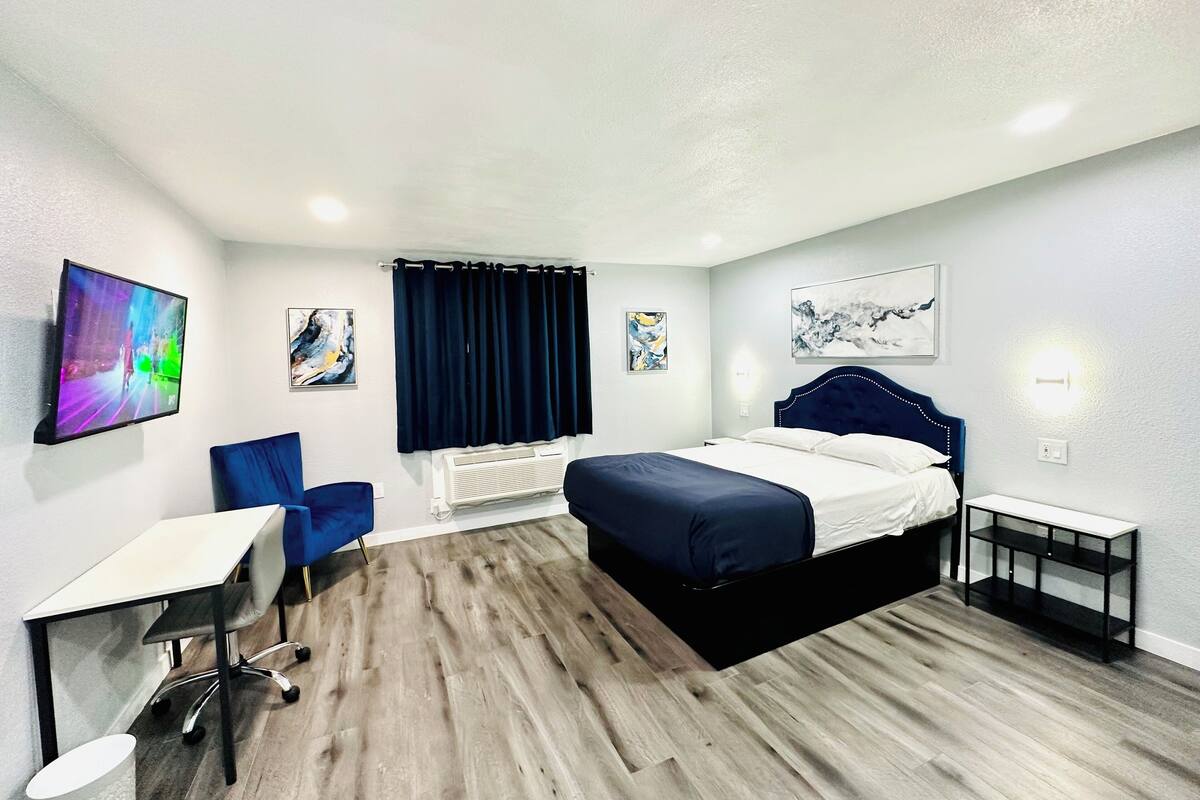A modern hotel room with a bed, a desk, a chair, and artwork on the walls.