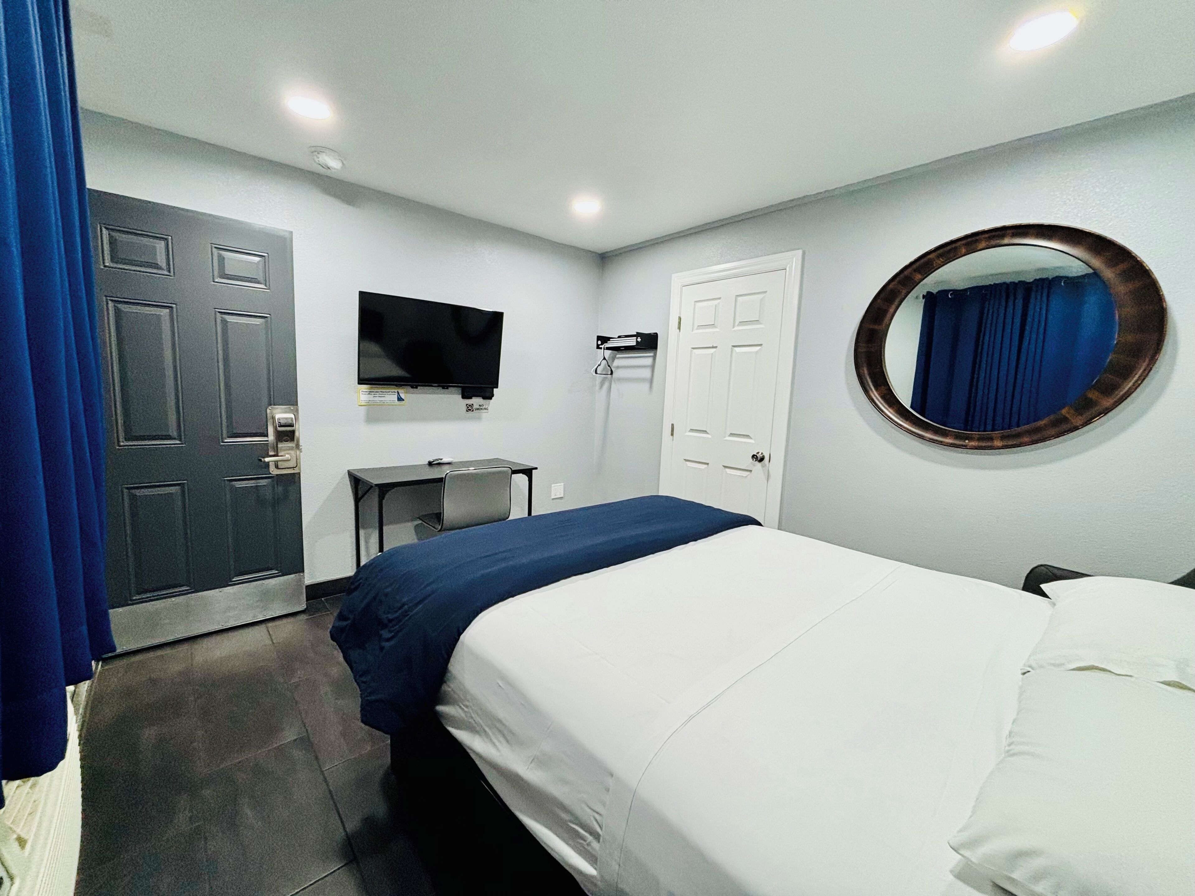 A hotel room with a bed, a desk, a television, a door, and a mirror.