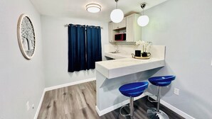 A bathroom with a white vanity, a mirror, a sink, and two blue bar stools. - Perfect Inn Motel (Las Vegas)