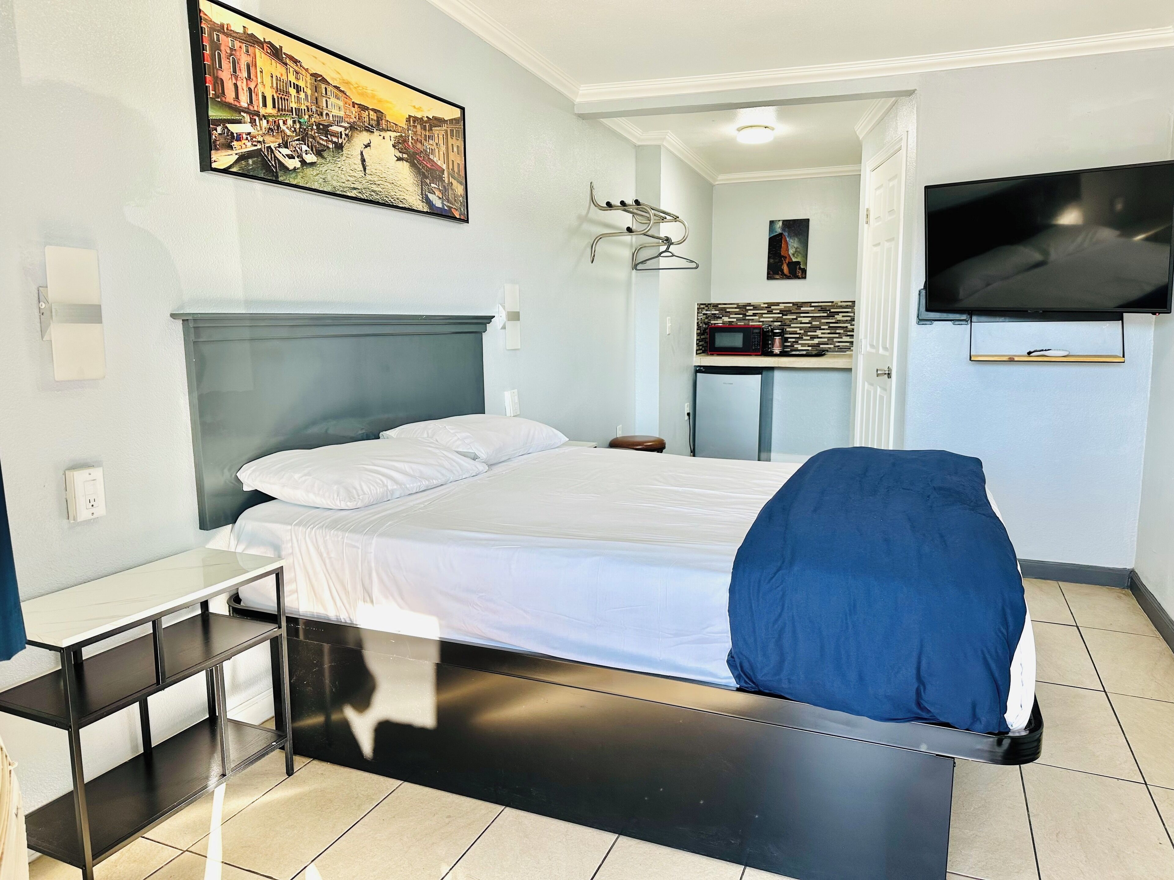 A hotel room with a bed, a TV, a painting, a microwave, and a small kitchenette.