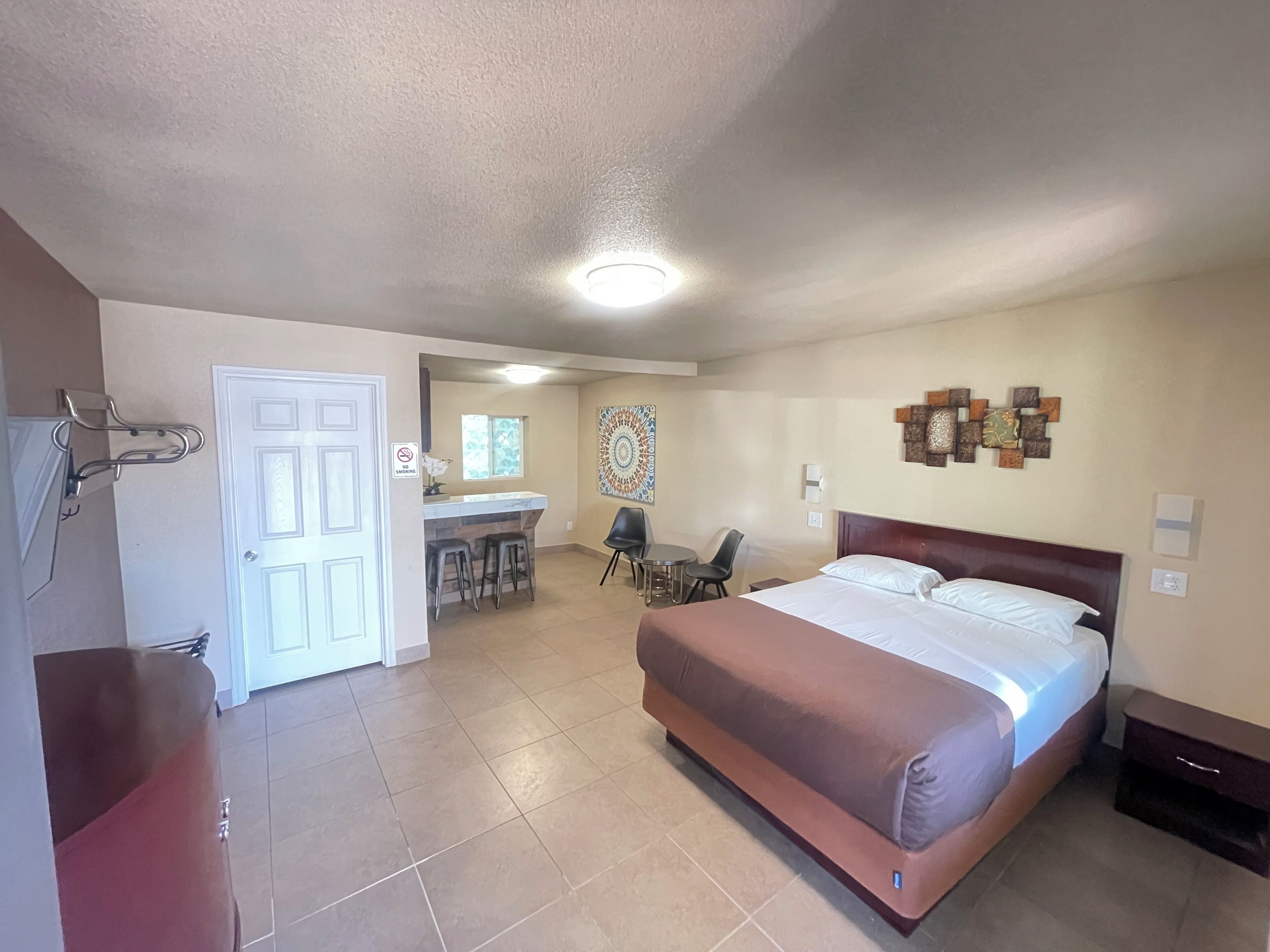 A hotel room with a large bed, a desk with two chairs, a small kitchen area, and a bathroom with a shower.
