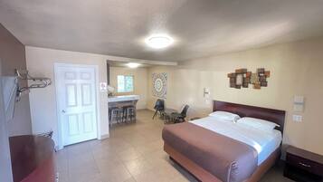 A hotel room with a large bed, a desk with two chairs, a small kitchen area, and a bathroom with a shower.