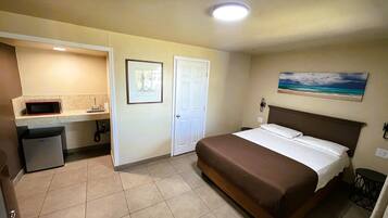 A hotel room with a bed, a small kitchenette, a bathroom, and a painting on the wall.