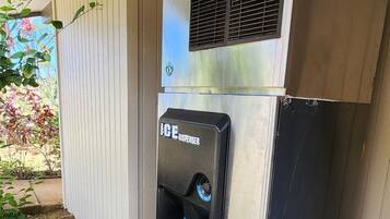 A portable ice dispenser attached to a metal cabinet, located outdoors against a wooden wall.