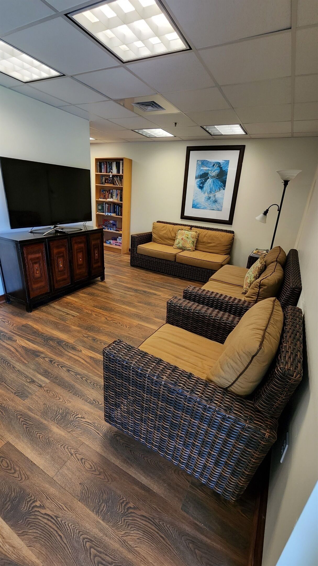 A living room with a flat-screen TV, a bookshelf, a framed painting, and a wicker sofa set.