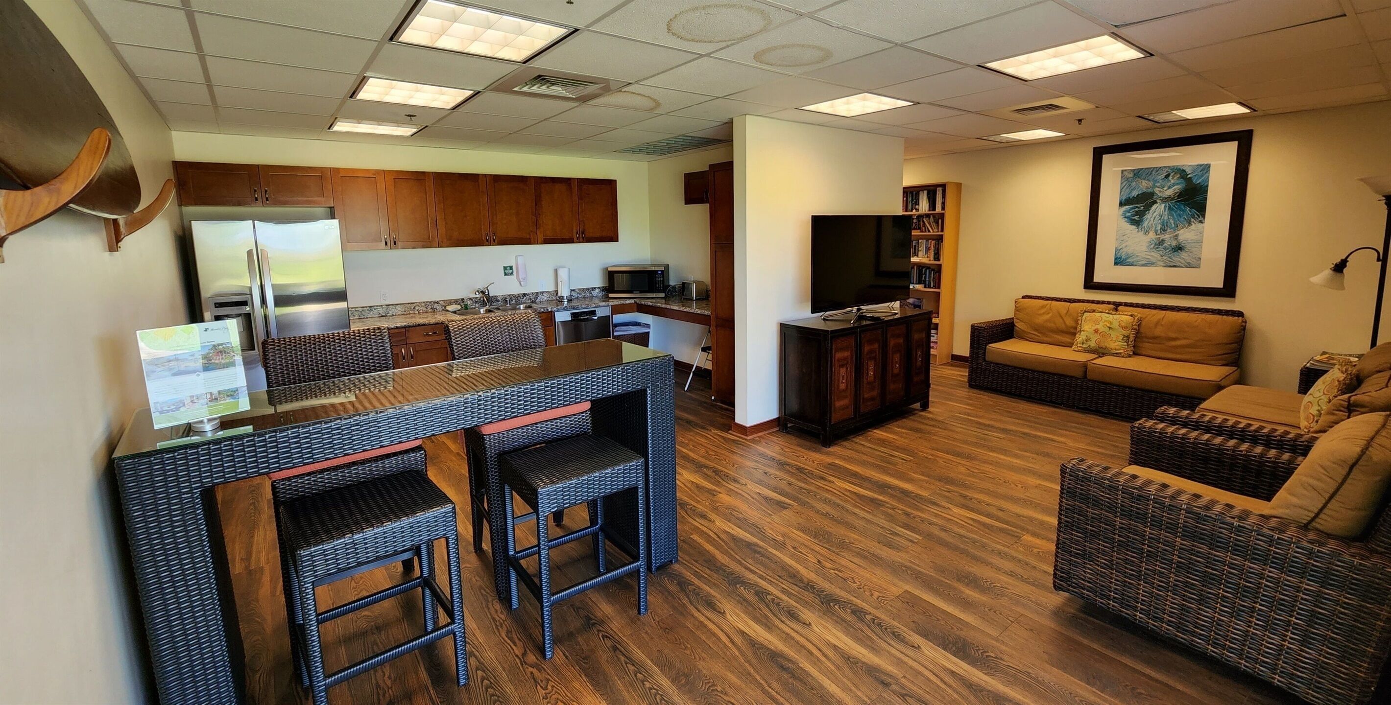A modern kitchen with stainless steel appliances, a dining area with wicker furniture, and a living room with a sofa and a flat-screen TV.
