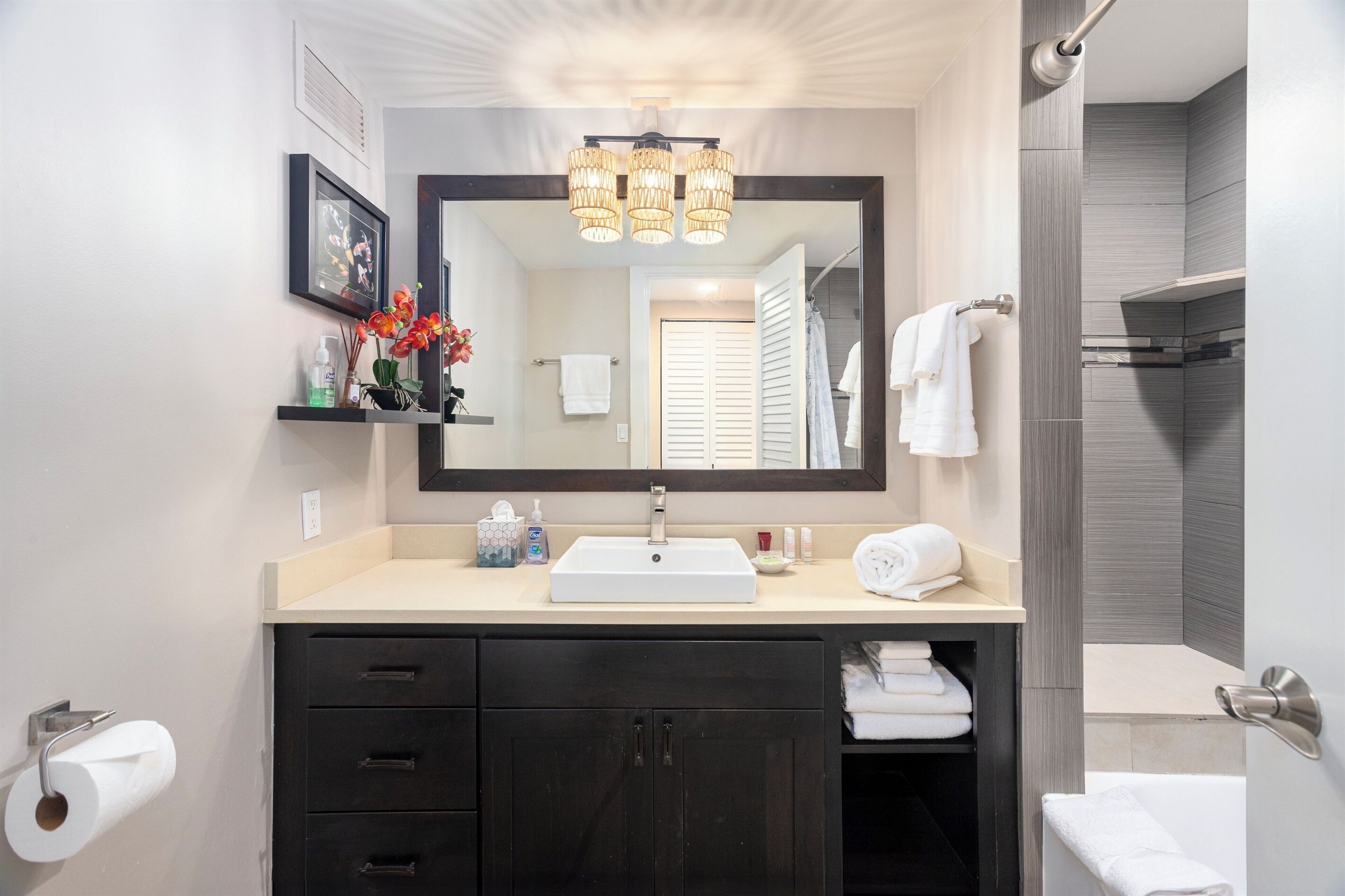 A modern bathroom with a large mirror, a sink, dark cabinets, and a shower area.