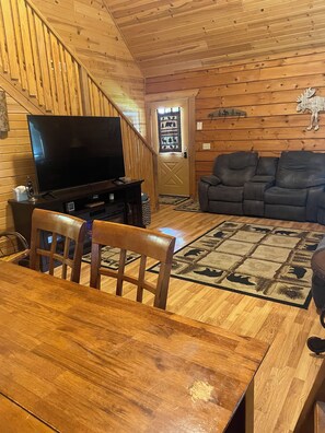 A wooden interior with a TV, sofa, dining table, and chairs.
