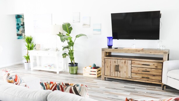 Una sala de estar moderna con un sofá blanco, un mueble de madera y un televisor en la pared.