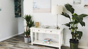Una consola blanca con una lámpara, una planta en maceta y un estante pequeño con libros.