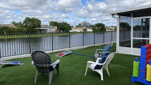 Un patio con césped artificial, dos sillas, una mesita y vistas a la piscina.