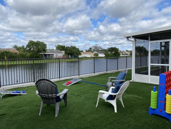 A patio with artificial grass, two chairs, a small table, and a pool view.