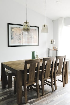A dining area with a wooden table and chairs, a pendant light, a framed artwork on the wall, and a small side table with a green pitcher and a white lantern. - Waterfront Boca Raton Home - Pets OK - Heated Pool (Boca Raton)