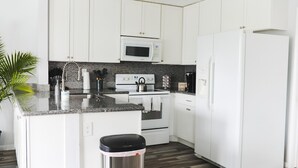 Una cocina moderna con armarios blancos, un lavamanos de acero inoxidable, un microondas, un horno y un refrigerador.