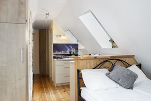 A bedroom with a sloped ceiling, a bed with white and gray bedding, a wooden headboard, and a view of a cityscape through a window. - Elite Apartments Długa Rooftop (Gdansk)