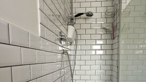 Ein Badezimmer mit weißen Fliesen im U-Bahn-Stil, einer Dusche mit Handbrause und einer gläsernen Duschkabine.