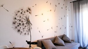 Ein modernes Wohnzimmer mit einer großen Wandmalerei von Löwenzahn, einem grauen Sofa mit Kissen und einem Holzesstisch.