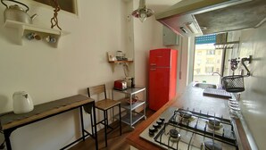 Eine kleine Küche mit einem Gasherd, einem roten Kühlschrank, einem Holztisch und einem Stuhl.