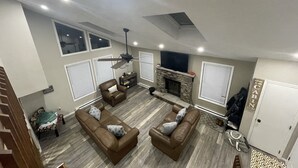 A spacious living room with a fireplace, two sofas, a ceiling fan, and a TV mounted above the fireplace. - Cozy, Relaxing, Getaway house in Big Bass community Poconos-3 mins walk to lake (Gouldsboro)