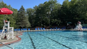 A swimming pool with clear blue water, surrounded by trees and equipped with blue lounge chairs and a red umbrella. - Cozy, Relaxing, Getaway house in Big Bass community Poconos-3 mins walk to lake (Gouldsboro)