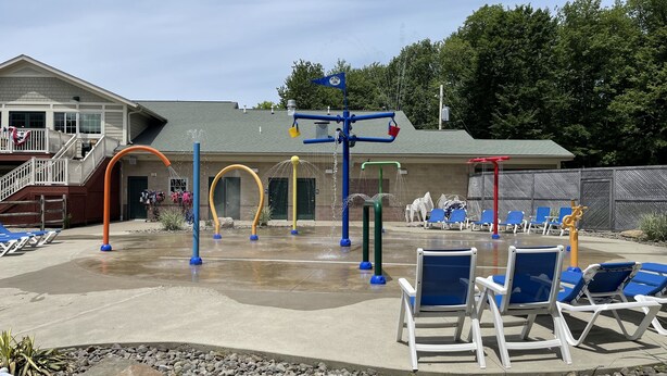 A water play area with slides and swings, surrounded by blue lounge chairs and a building with a staircase. - Cozy, Relaxing, Getaway house in Big Bass community Poconos-3 mins walk to lake (Gouldsboro)