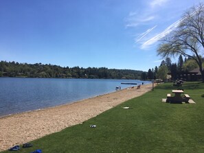 A lakeside park with picnic tables, a sandy beach, and a grassy area.