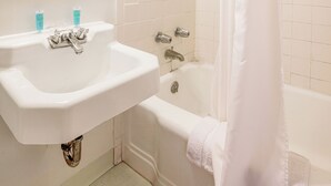 A bathroom with a white sink, a mirror with a mosaic frame, a shower curtain, and a bathtub. - Cadiz Motel by OYO on Route 250 (Cadiz)