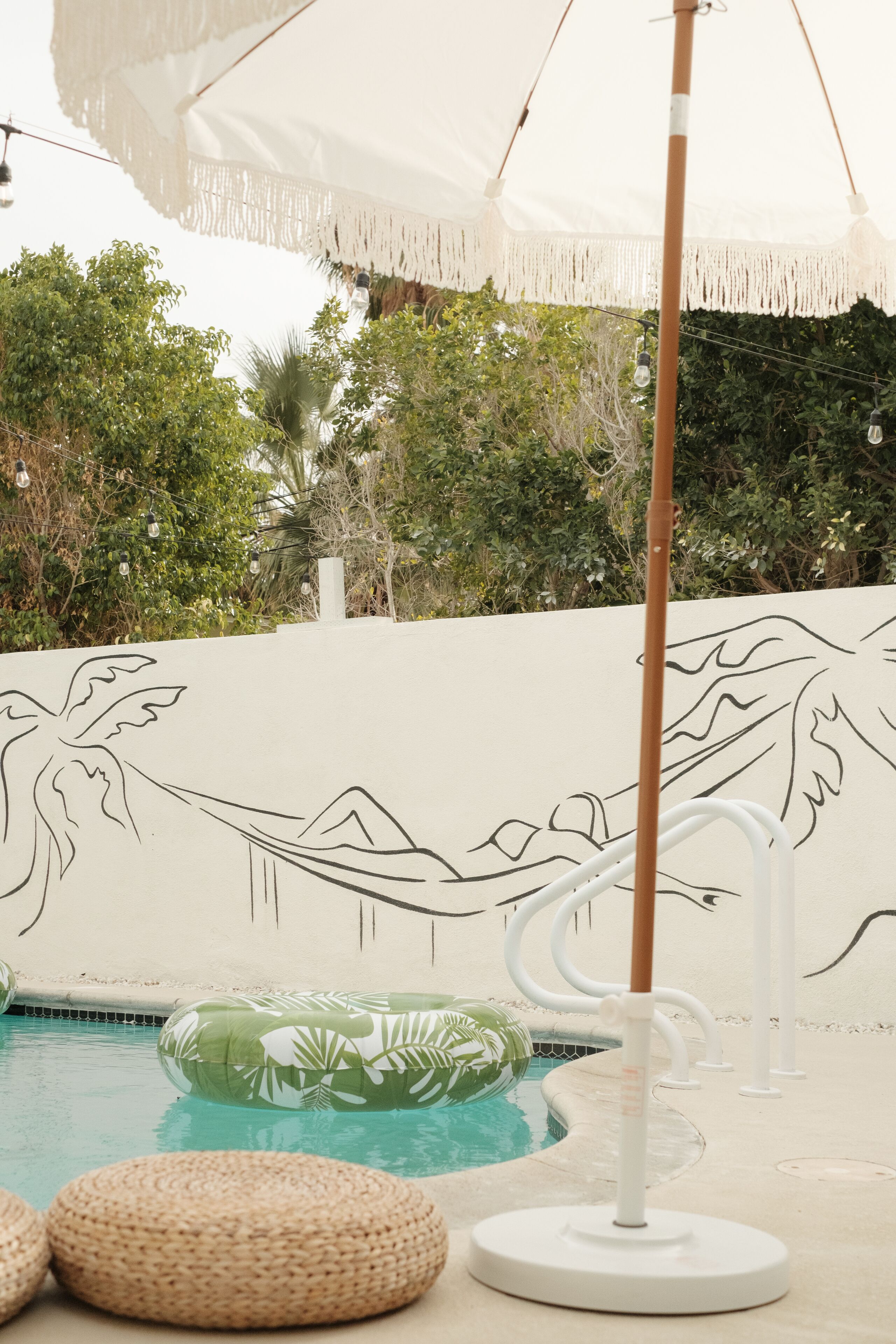 Une piscine agrémentée d’un parasol blanc, d’un hamac et d’une fresque représentant des palmiers et des montagnes.