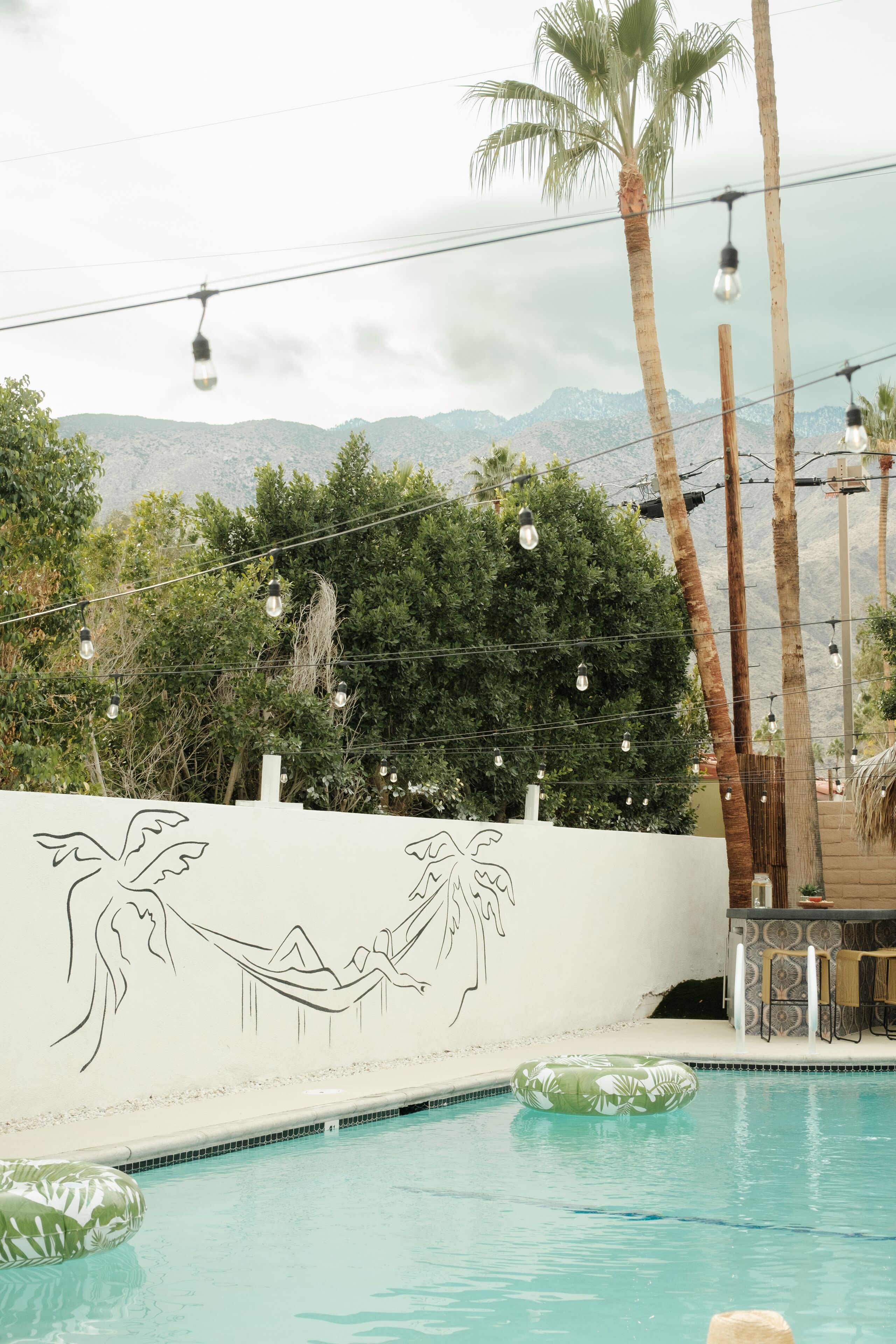 A swimming pool with a mural of a hammock and palm trees, surrounded by greenery and a mountainous backdrop.