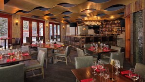 A restaurant with wooden tables and chairs, a bar area, and a view of trees through large windows. - Luxury 3-Bedroom Penthouse-style Retreat in Beaver Creek Village (Beaver Creek)